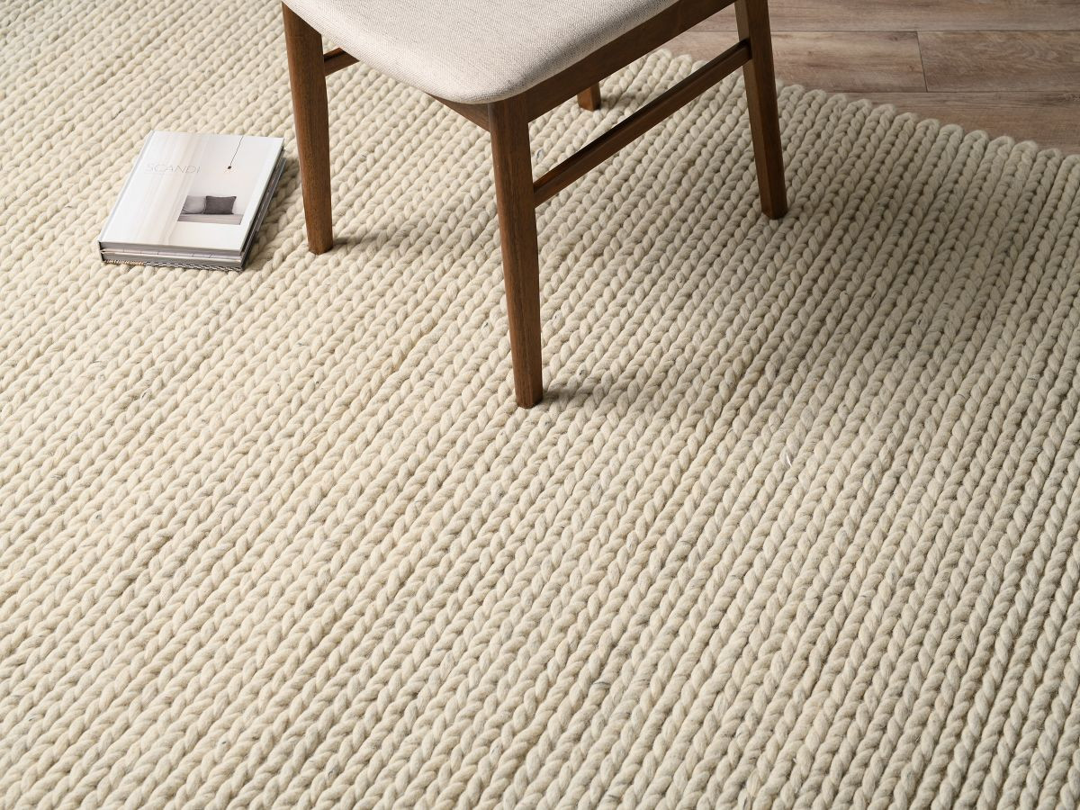A chair and a book casually placed on top of a large white braided wool rug.