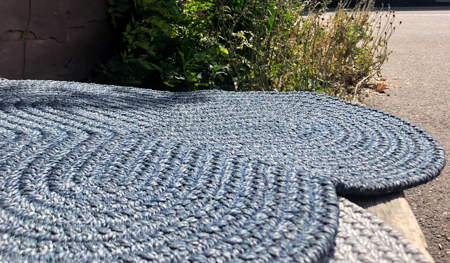 Braided wool rugs laying outside in the fresh air of a driveway to dry after a cleaning.