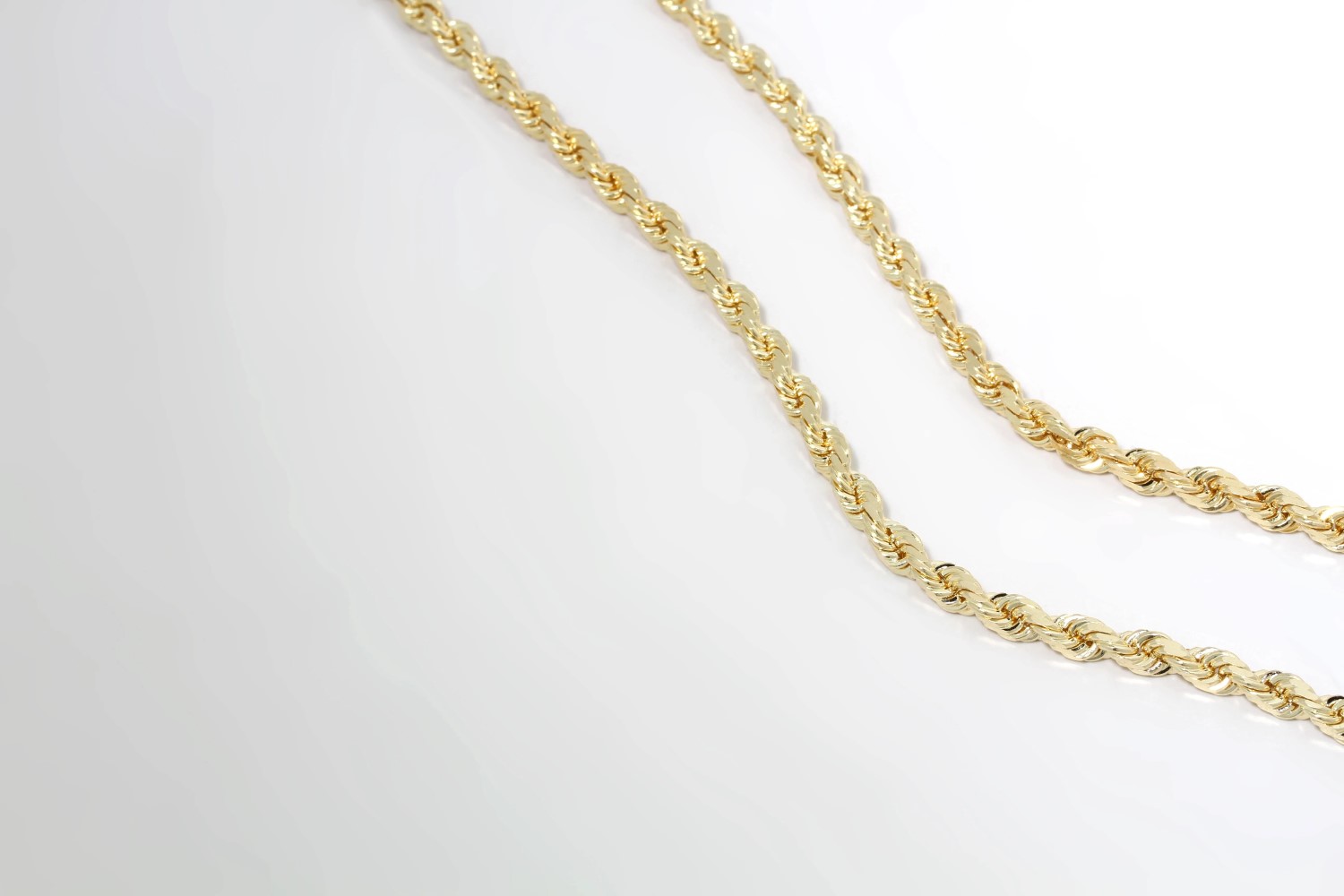 Two gold rope chains on display above a white backdrop. They are thin and intricate.