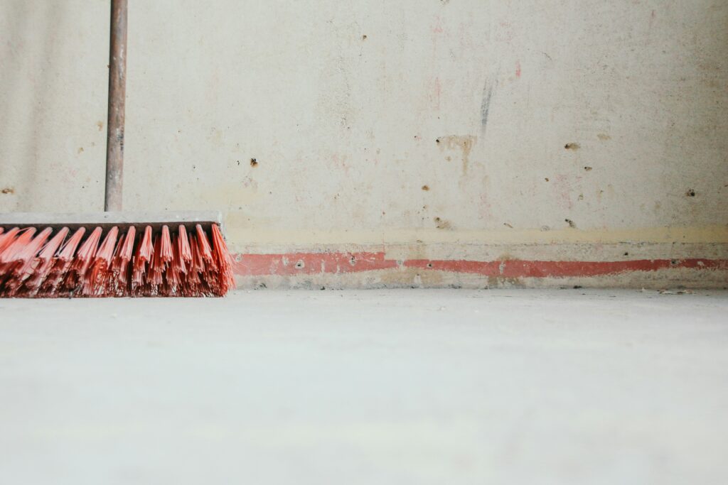 A broom is shown resting against a wall. 