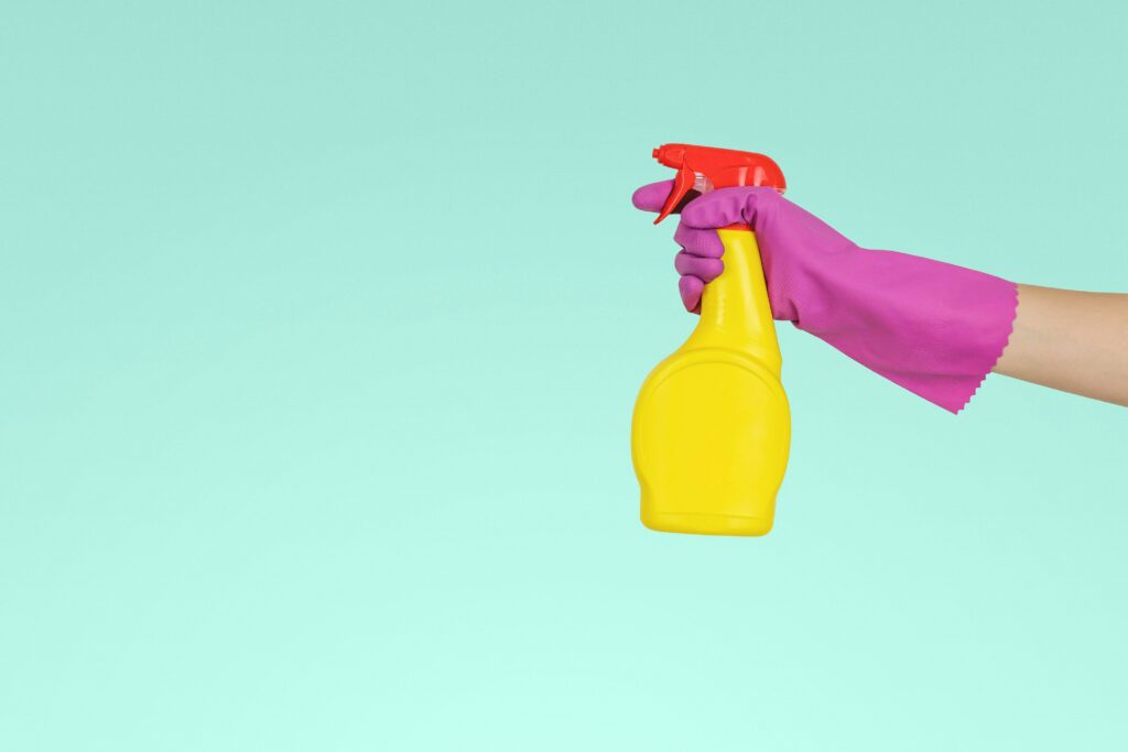 An cleaning solution is being held up in front of a mint green background.
