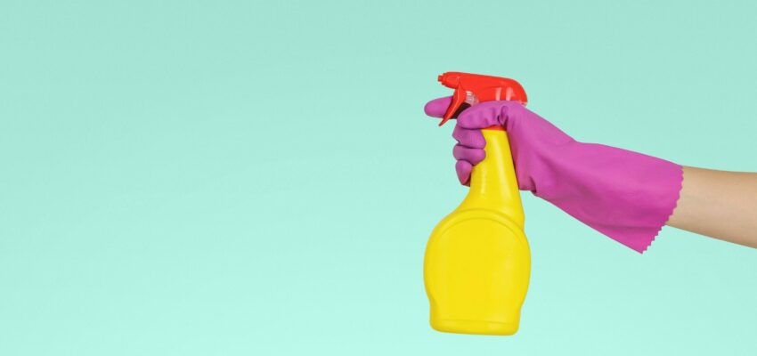 An cleaning solution is being held up in front of a mint green background.