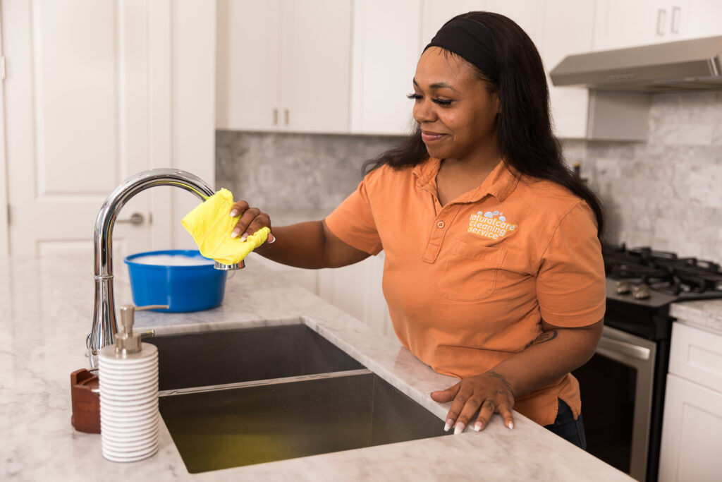 A Naturalcare Cleaning Service maid is offering affordable cleaning services in a client's kitchen.