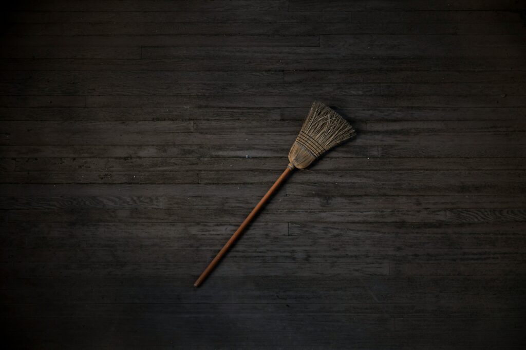 A broom is laying on a dark wood floor.