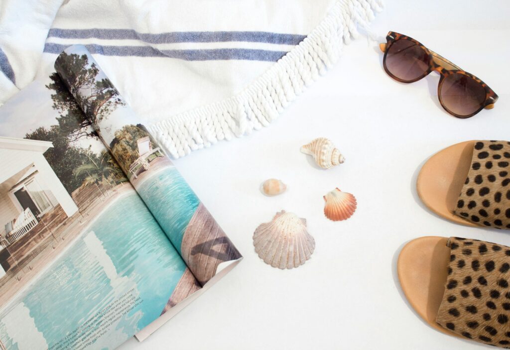 Objects that represent Summer: flip flops, sunglasses, a travel magazine, sea shells, and a beach towel. This is the time to enjoy the weather while we perform cleaning services Sugar Land!