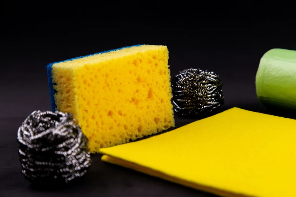 An array of sponges and scrubbers on a black background. You don't need to supply tools like this when hiring cleaners before move in.