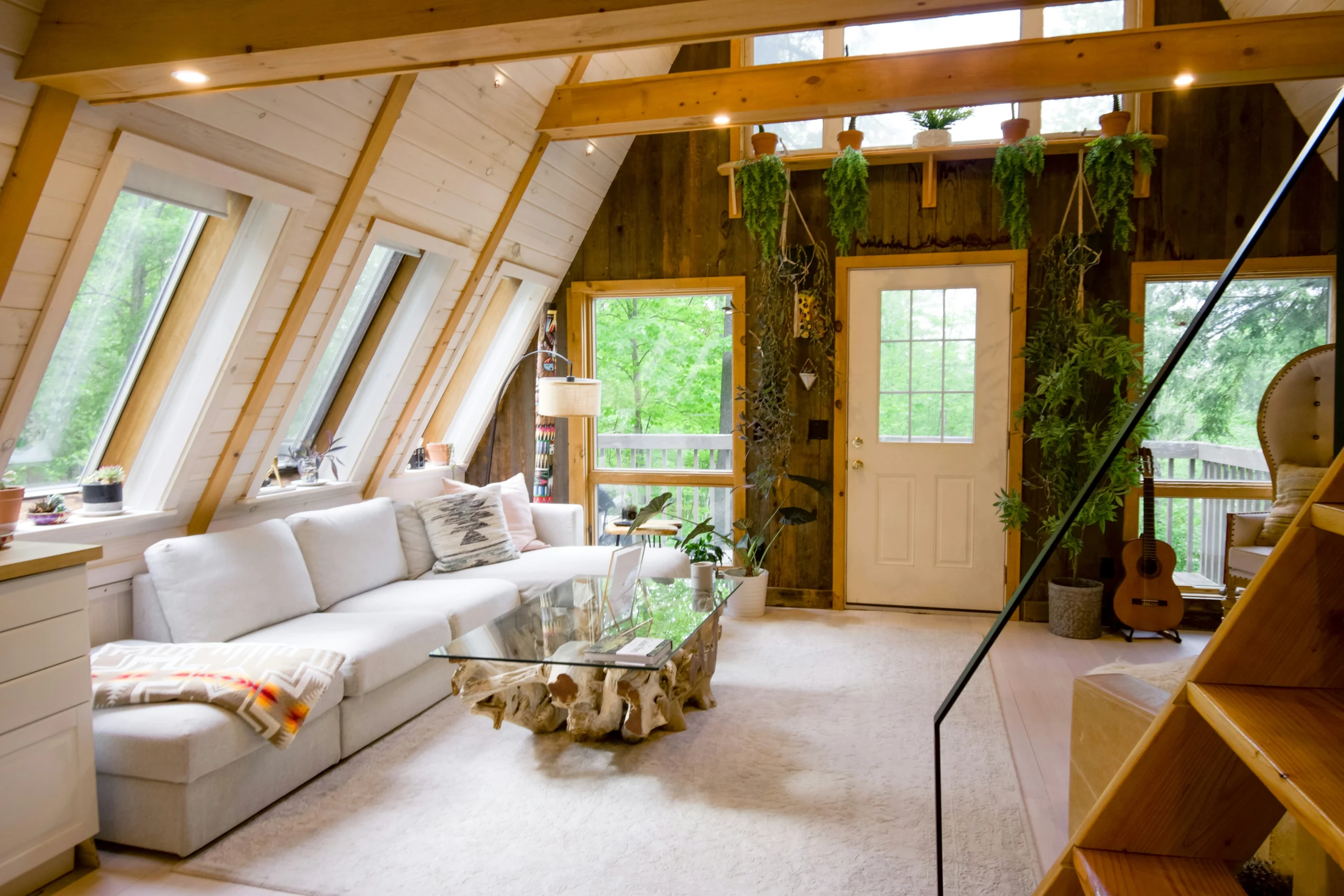 A freshly cleaned Airbnb cabin's living room. A white couch and white carpet contrast with the earthy woods outside. People who stay in a rental like this wonder how much do you tip Airbnb cleaners.