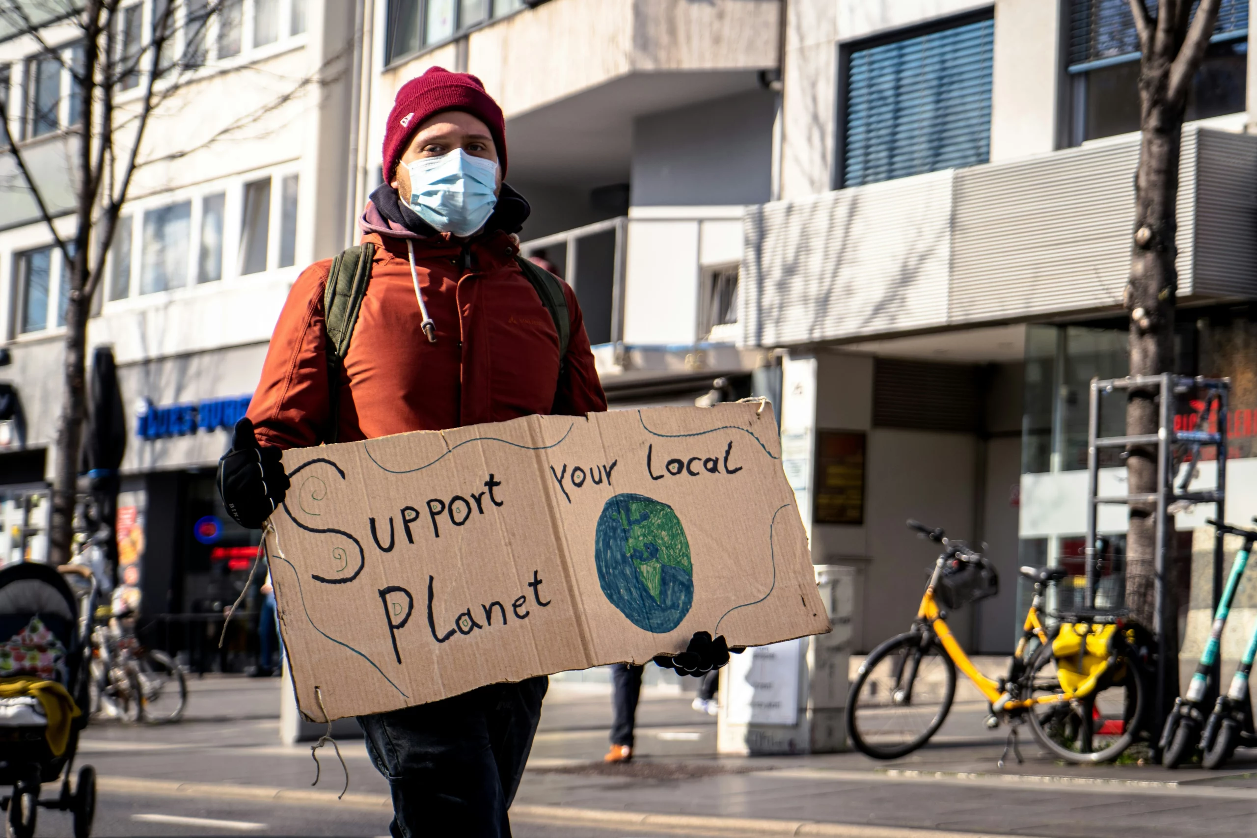 A man is holding a sign that says 'support your local planet'. He wants more people to use green cleaners and go green with eco friendly cleaning solutions.