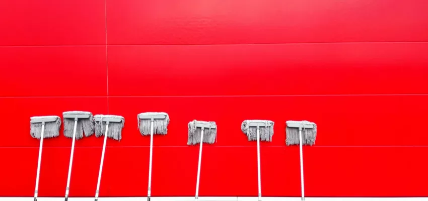 White mops left dripping against a red brick wall to dry. Whether you get deep cleaning vs move out cleaning, mopping is essential.