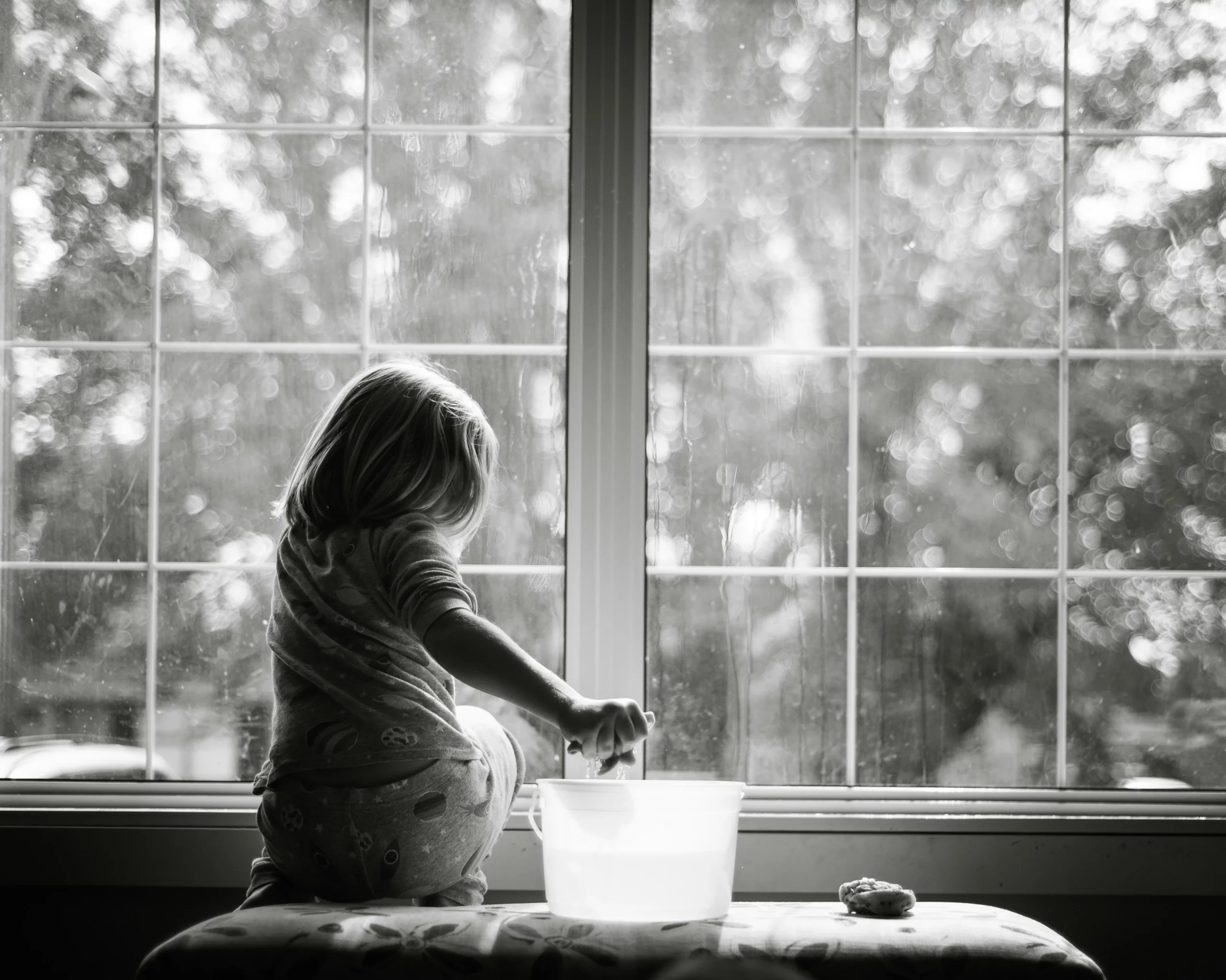 A little girl is washing a window in a greyscale image. ADHD cleaning tips include getting the whole family on board!
