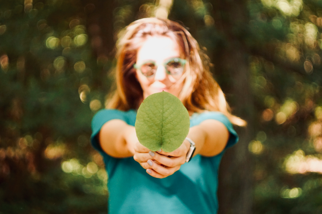 A girl is holding a leaf in front of her, which is in focus.