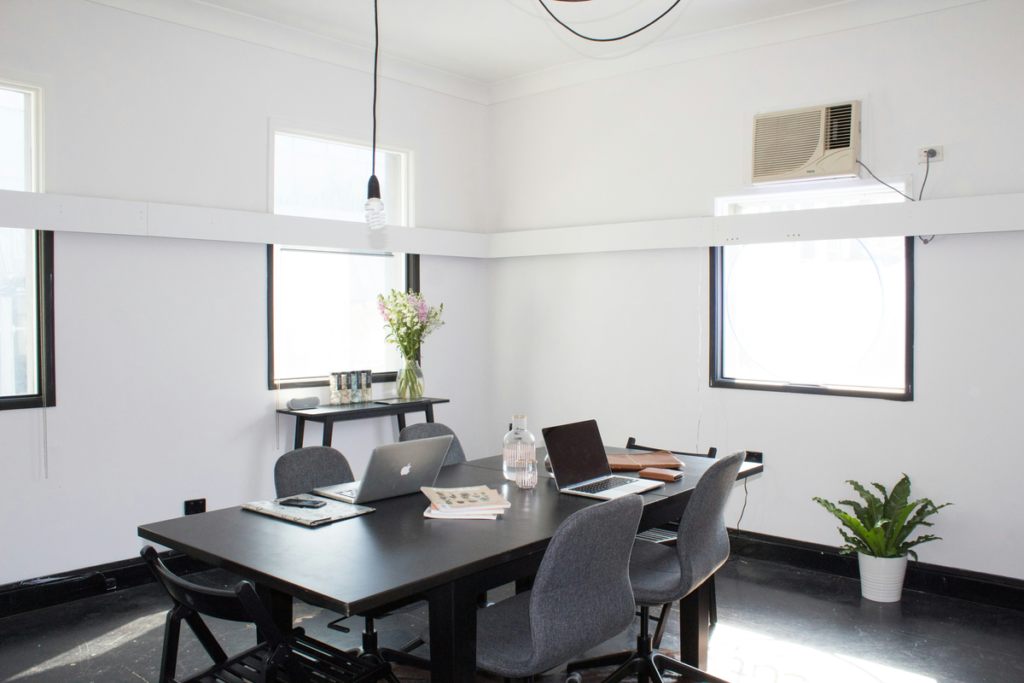 A bright office space in the summertime is letting light in. Potted plants are growing in the window after some office cleaning tips were used.