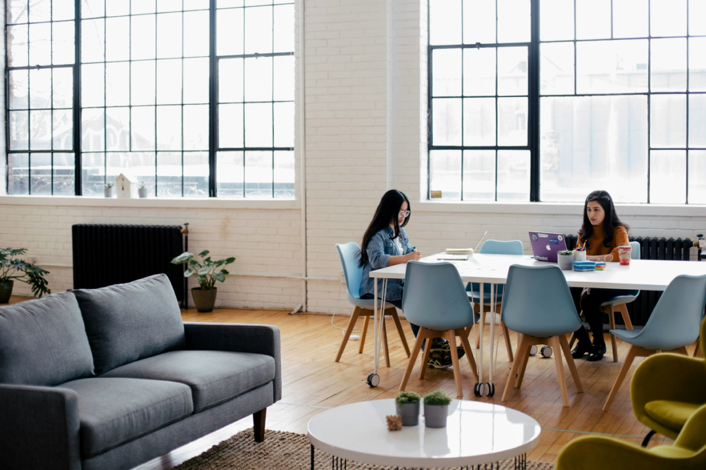 Two young professionals work on laptops in a coworking space. They're benefitting from using office cleaning tips to improve their workspace.