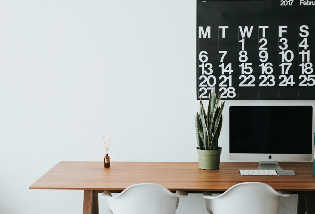 A large calendar hangs above an office desk to track weekly office cleaning tips.